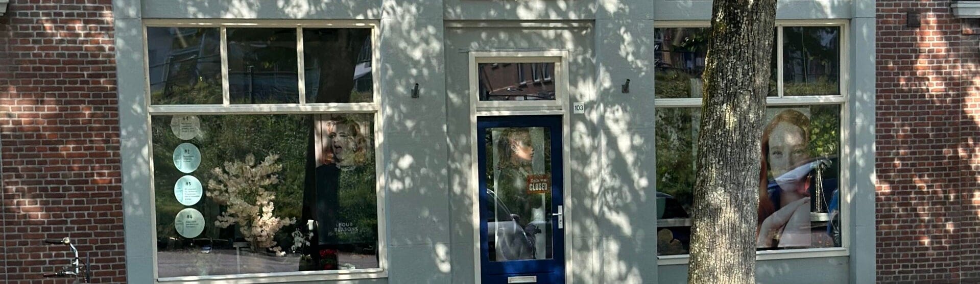 De gevel van Beautylounge Rotterdam aan de Oostzeedijk Beneden, met de blauwe voordeur en bladschaduw op de lichte pui.