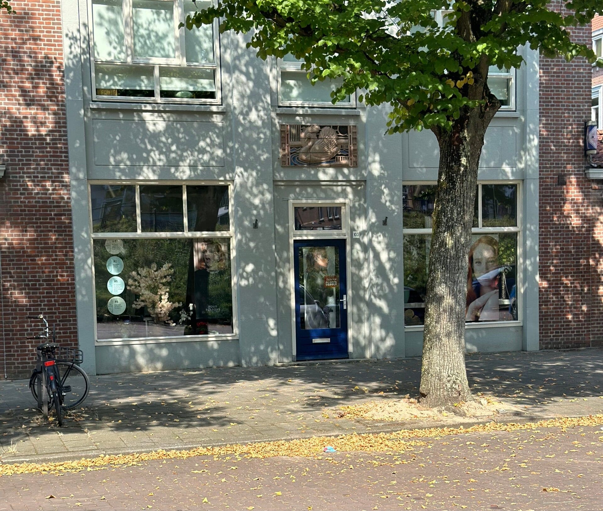 De blauwe voordeur van de salon, met de reliëftegel erboven in de lichte gevel.